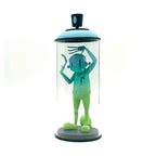Green character figurine inside a transparent cylindrical container with a black lid on a white background