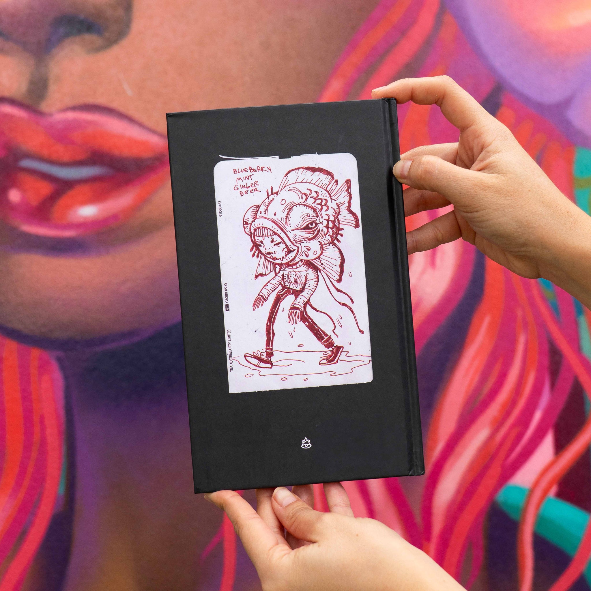 Black book with a red illustration held by hands against a colorful background