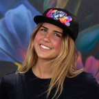 Woman wearing a black cap with colorful designs against a vibrant, abstract background
