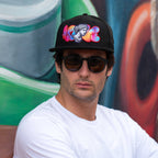 Man wearing a colorful cap and sunglasses in front of a graffiti wall