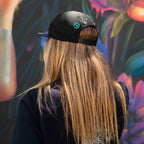 Person wearing a black cap with peace signs, standing in front of a colorful floral mural.
