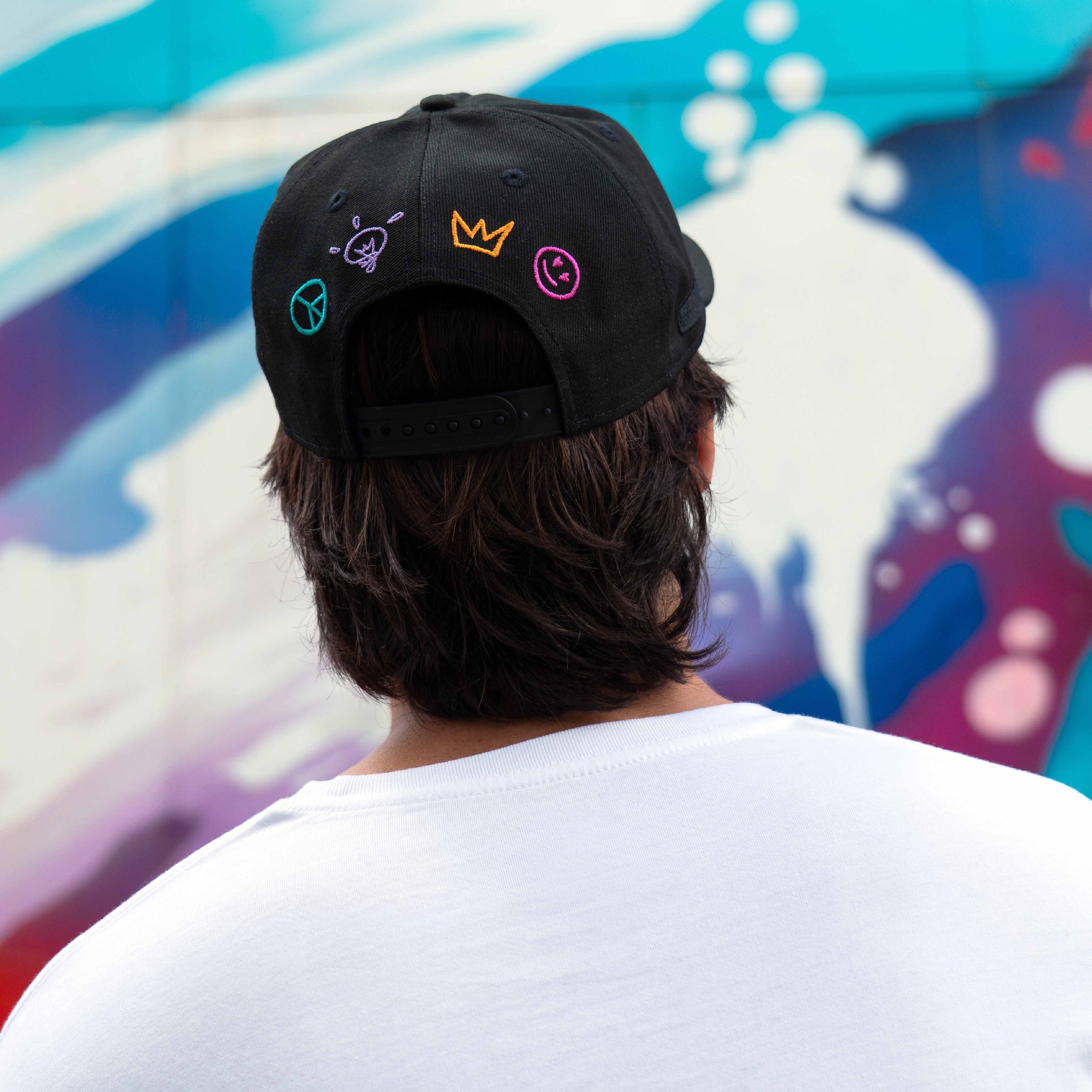 Person wearing a black cap with colorful symbols against a colorful abstract background