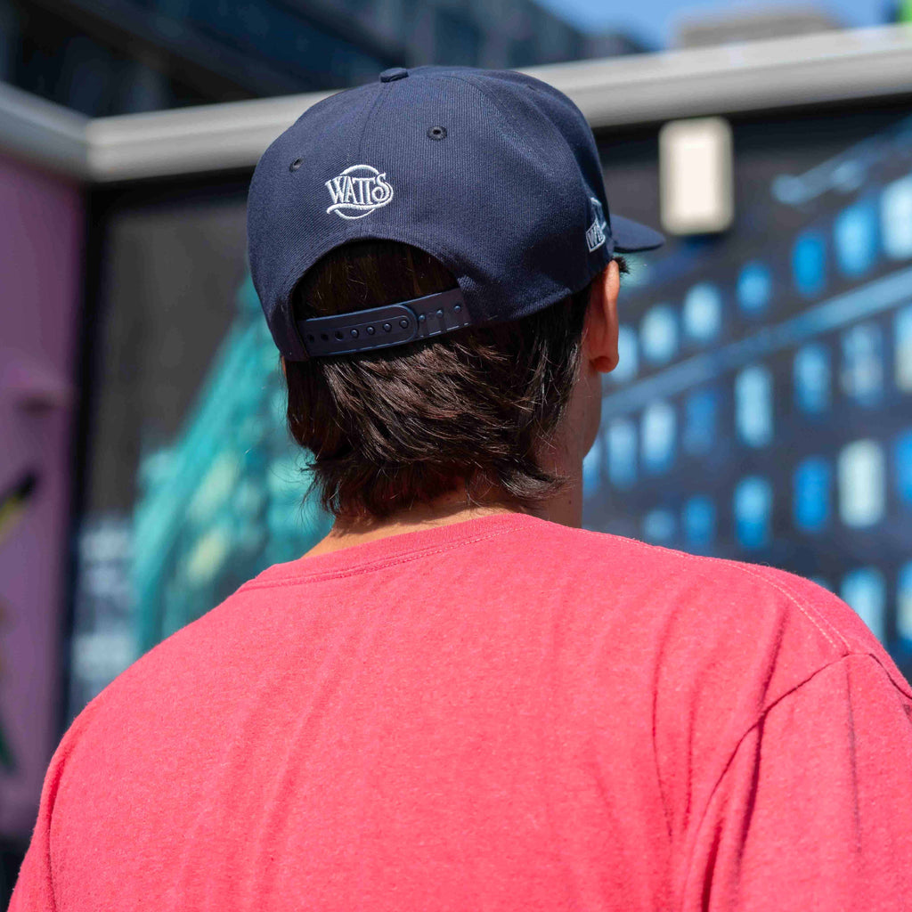 Person wearing a navy cap with a logo, facing away from the camera with a colorful background.