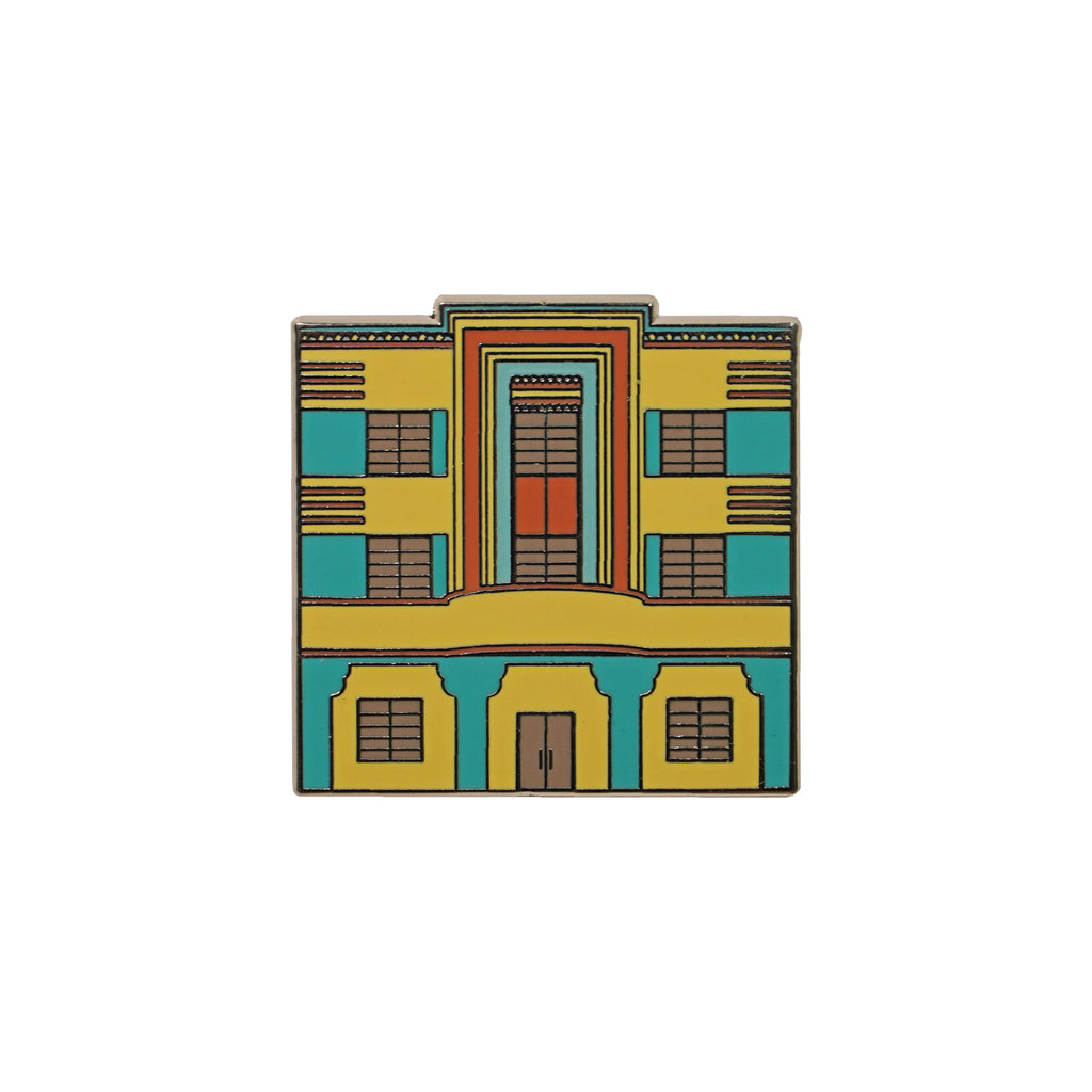 Colorful enamel pin shaped like an Art Deco building in yellow, teal, and orange